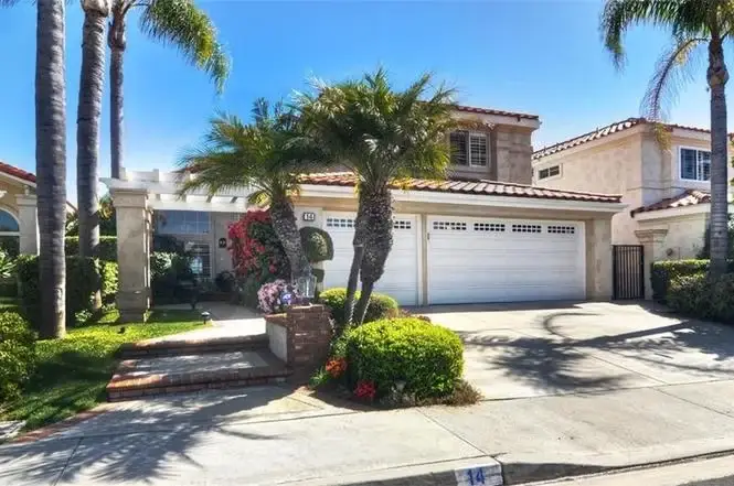 California real estate house with two stories, white garage door, palm trees, and colorful landscaping