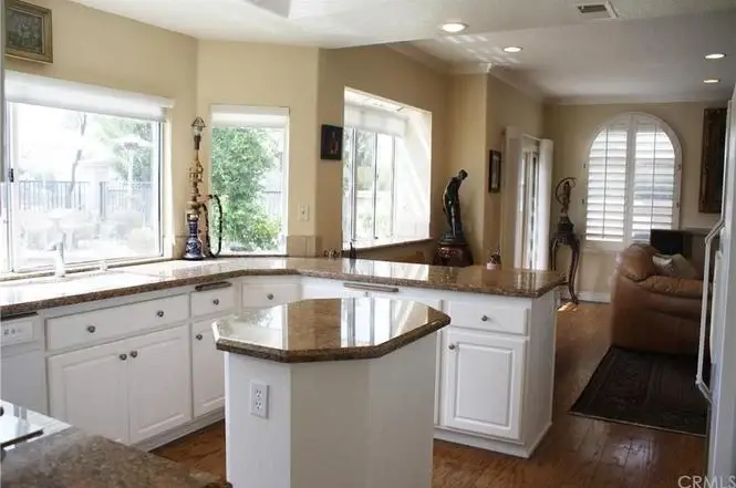 Kitchen with granite countertops, white cabinets, windows, and living area in background