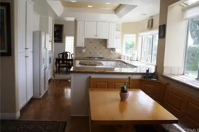 Kitchen with wooden cabinets, large island with seating, windows, dining table, and appliances
