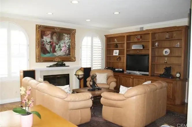 Living room with two beige leather chairs, wooden entertainment center, TV, painting, and fireplace