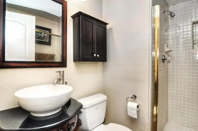 Bathroom with shower, sink with dark wood cabinet, mirror, toilet, and towel holder