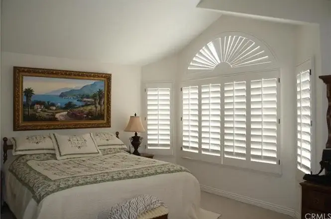 Bedroom with large painting, white walls, and shuttered windows with decorative arch