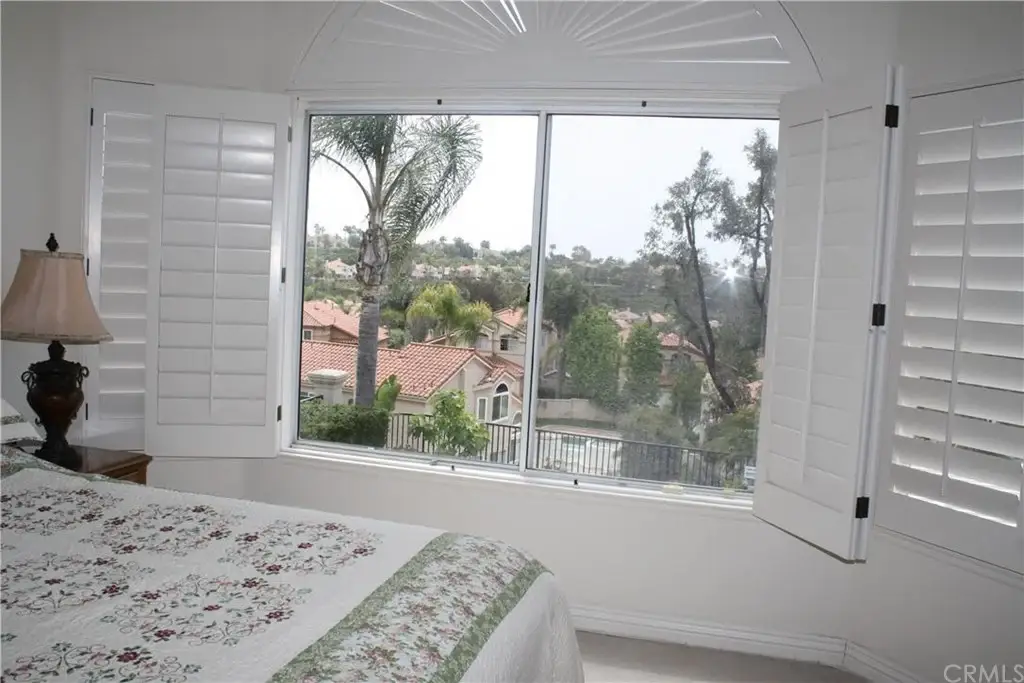 Bedroom with bed, floral bedding, lamp, and view of trees and hillside houses
