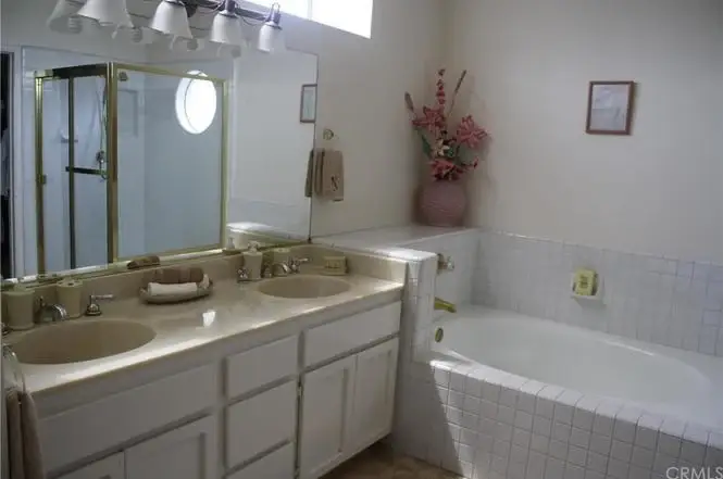 Bathroom with double sinks, large mirror, and bathtub with floral decorations