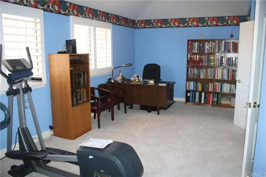 Room with blue walls, desk with lamp and chair, bookshelf, exercise equipment,