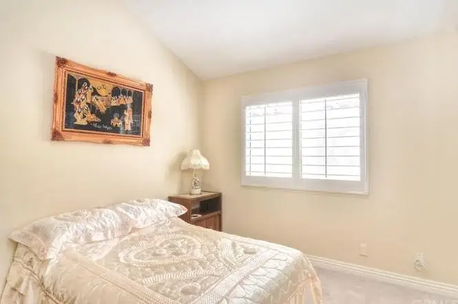 Bedroom with bed, cream bedspread, nightstand with lamp, artwork, and window