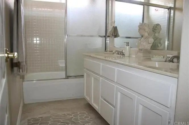 Bathroom with shower and bathtub, double sink vanity with beige countertops, white cabinets, and decorative figures