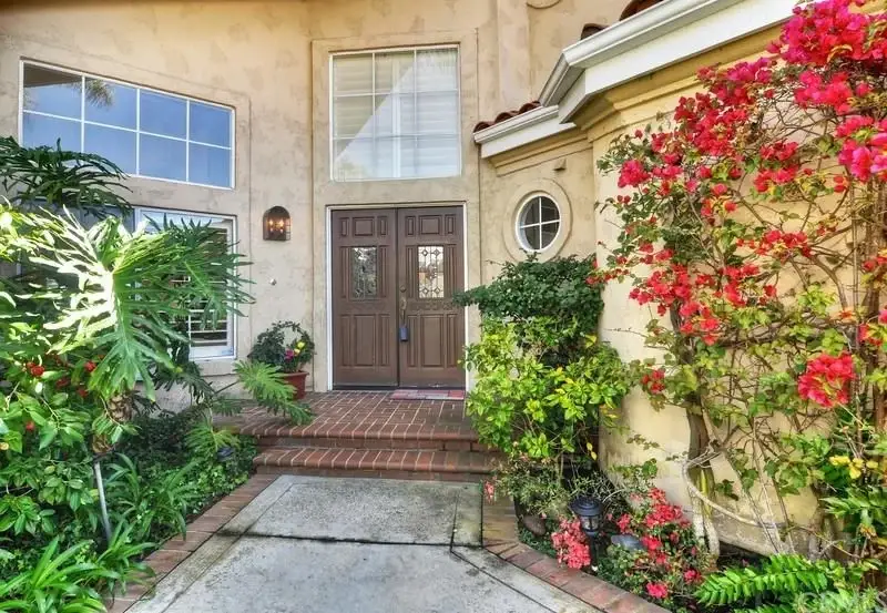 House entrance with double wooden doors and surrounding flowers and greenery