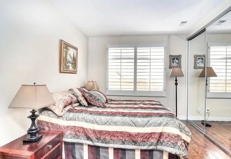 Bedroom with bed, decorative bedding, bedside lamps, mirrored closet, framed pictures, and window