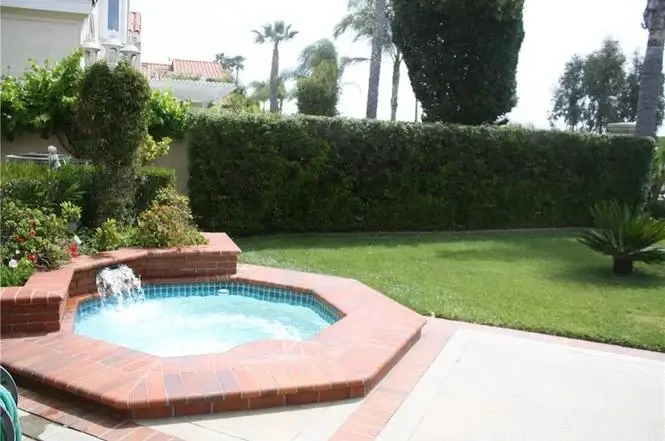 Outdoor hot tub next to lawn, hedges, and palm trees