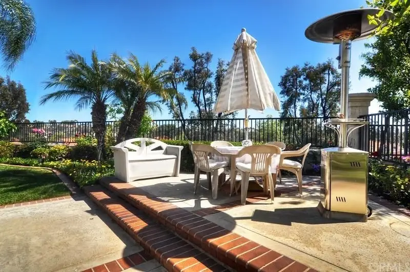 Patio with table, chairs, umbrella, heater, and landscaping with palm trees and flowers