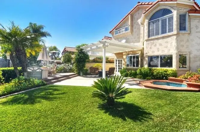 Luxurious house California real estate with landscaped backyard, lawn, palm trees, and patio with outdoor furniture