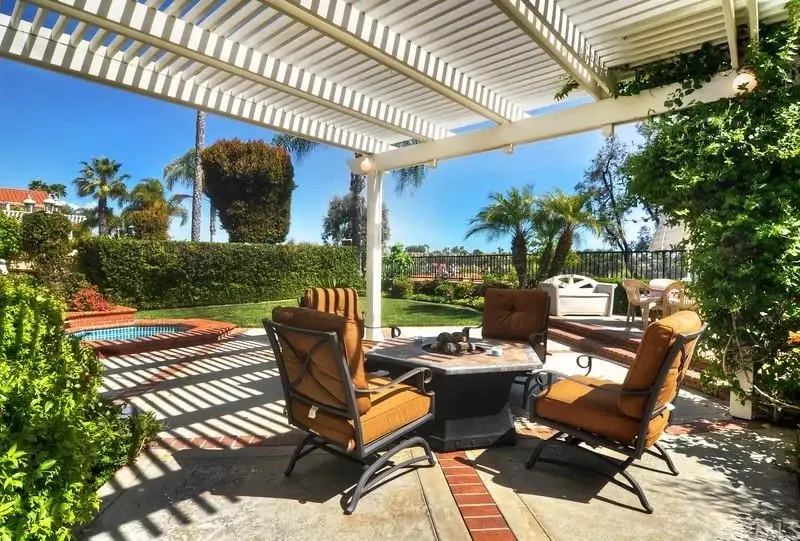 Outdoor patio with seating around fire pit, greenery, and swimming pool in background