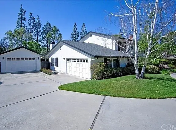 House California real estate with green lawn, trees, driveway, and two-car garage