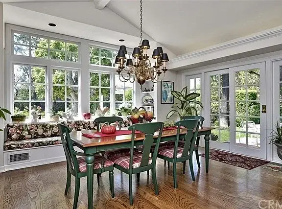 Dining area with large table, green chairs, chandelier, fruit decorations, windows, and plants