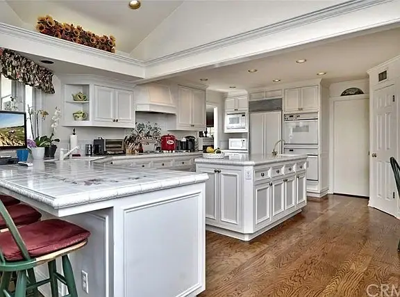 Kitchen with white cabinets, marble countertop, island with bar seating, appliances, and hardwood floor