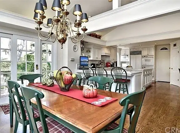 Dining area with wooden table, green chairs, chandelier, fruit decorations, and French doors