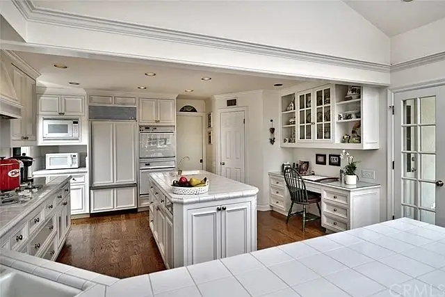 Kitchen with white cabinets, large island, fruit bowl, desk, and chair