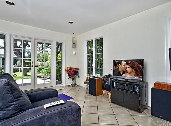 Living room with large sofa, TV, windows, flowers, and tiled floor