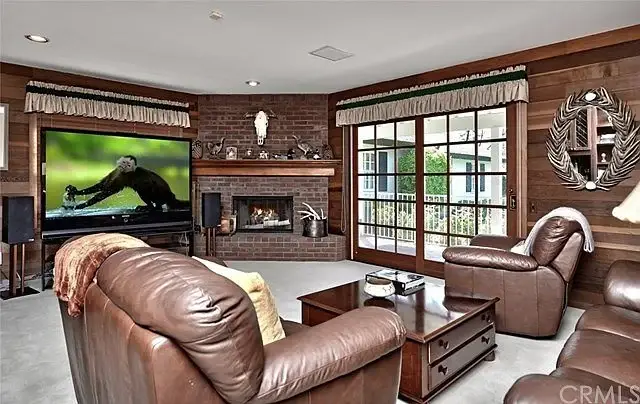 Living room with dark wood paneling, fireplace, leather armchairs, TV, and glass doors to outdoors