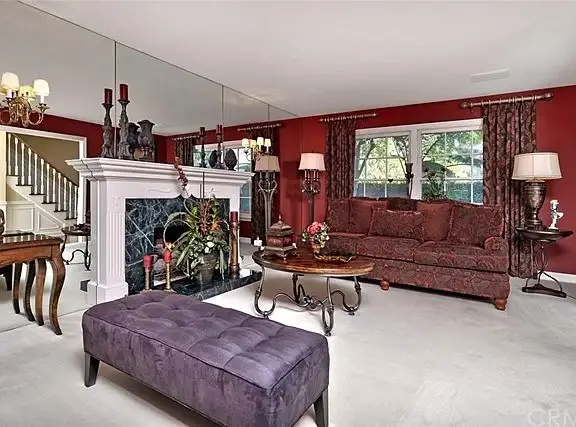 Living room with red wall, purple bench, chandelier, and fireplace decorations
