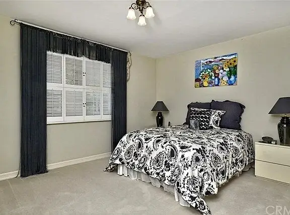 Bedroom with bed, black and white comforter, nightstands with lamps, artwork, beige walls, and carpet