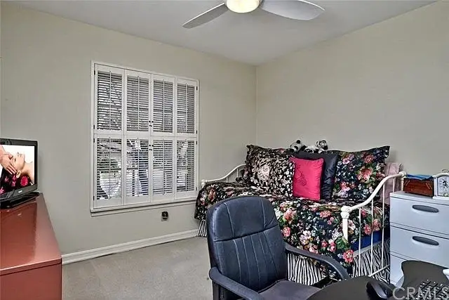 Bedroom with daybed, floral bedding, pink pillows, desk with chair, and TV on red cabinet