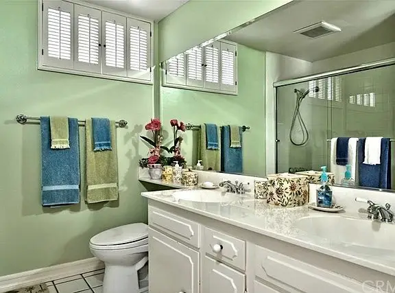Bathroom with green walls, white countertop, sink, mirror, towels, and glass shower