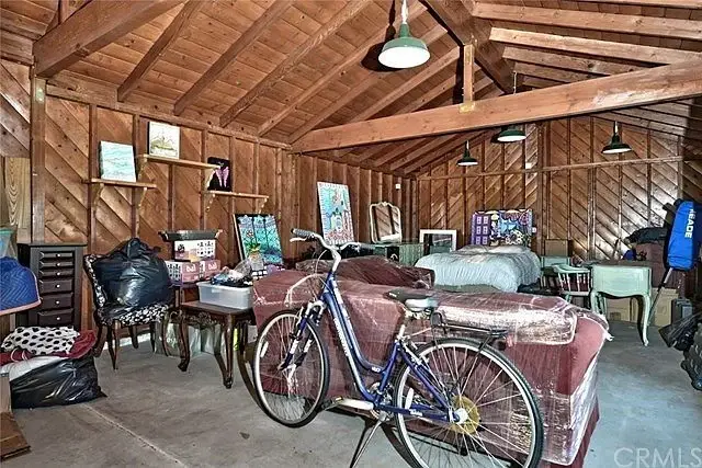 Garage with wooden beams, bicycle, covered furniture, and scattered items