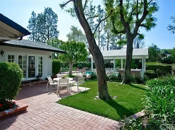 Backyard with patio table, chairs, greenery, trees, and pool area