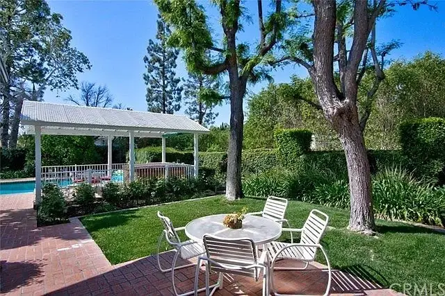 Backyard with patio table, chairs, greenery, trees, and swimming pool