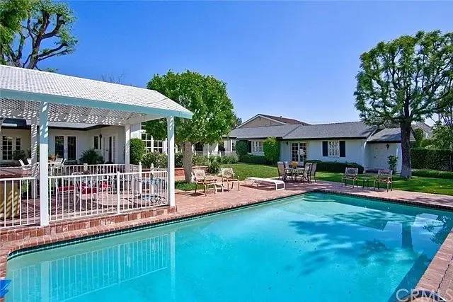 Backyard with swimming pool, greenery, covered patio, seating, and sun loungers