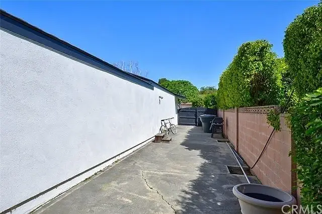 Pathway along side of house with concrete surface, fences, and greenery