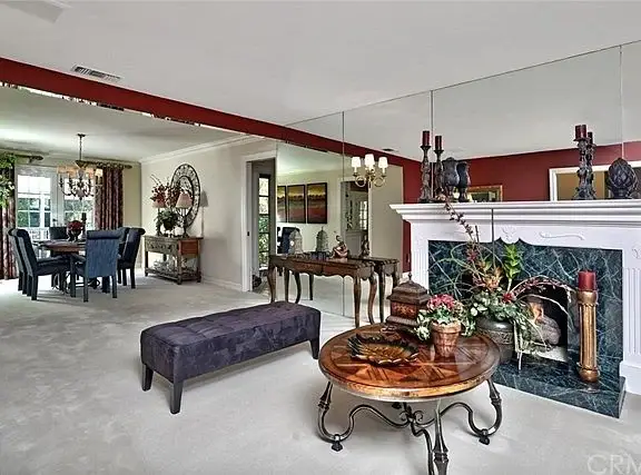 Living room with fireplace, coffee table, seating, plants, and dining area in background