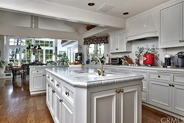 Kitchen with white cabinets, large island, appliances, windows, and plants