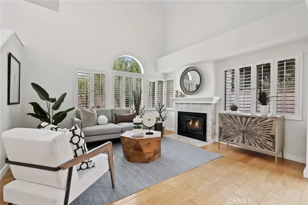 Living room with curved window, fireplace, gray sofa, accent chair, coffee table, and plants