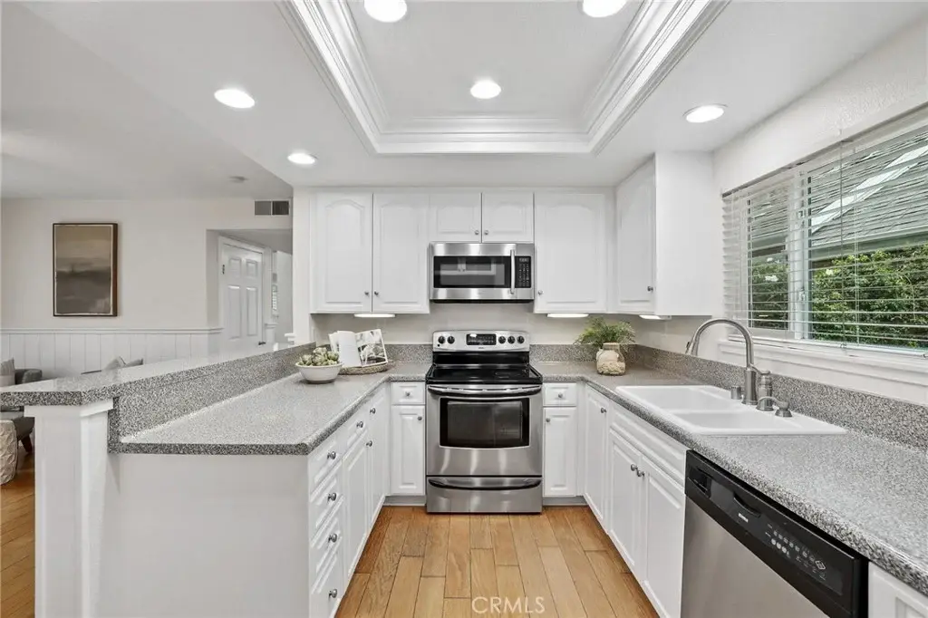 Kitchen with white cabinets, stainless steel oven and microwave, sink, granite countertops, and window