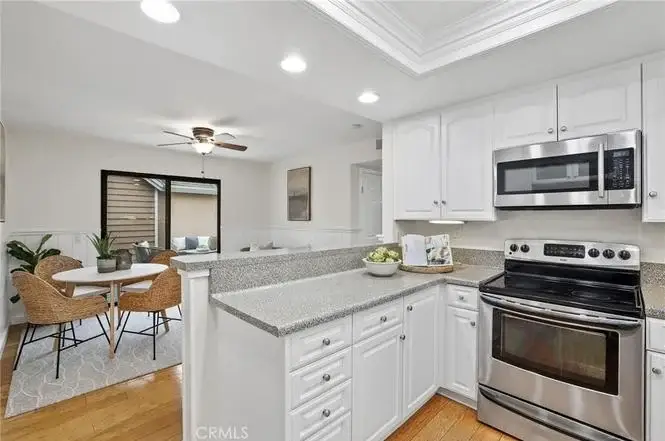 Kitchen with granite countertops, stainless steel appliances, white cabinets, and dining area with round table and four chairs