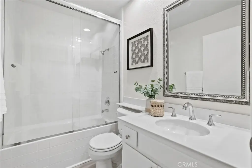 Bathroom with glass shower, white vanity, silver fixtures, plant, and artwork