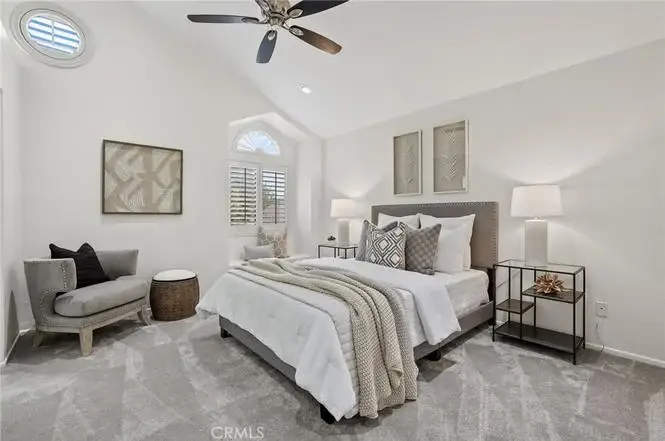 Bedroom with plush bed, neutral pillows, throw, lamps, and ceiling fan