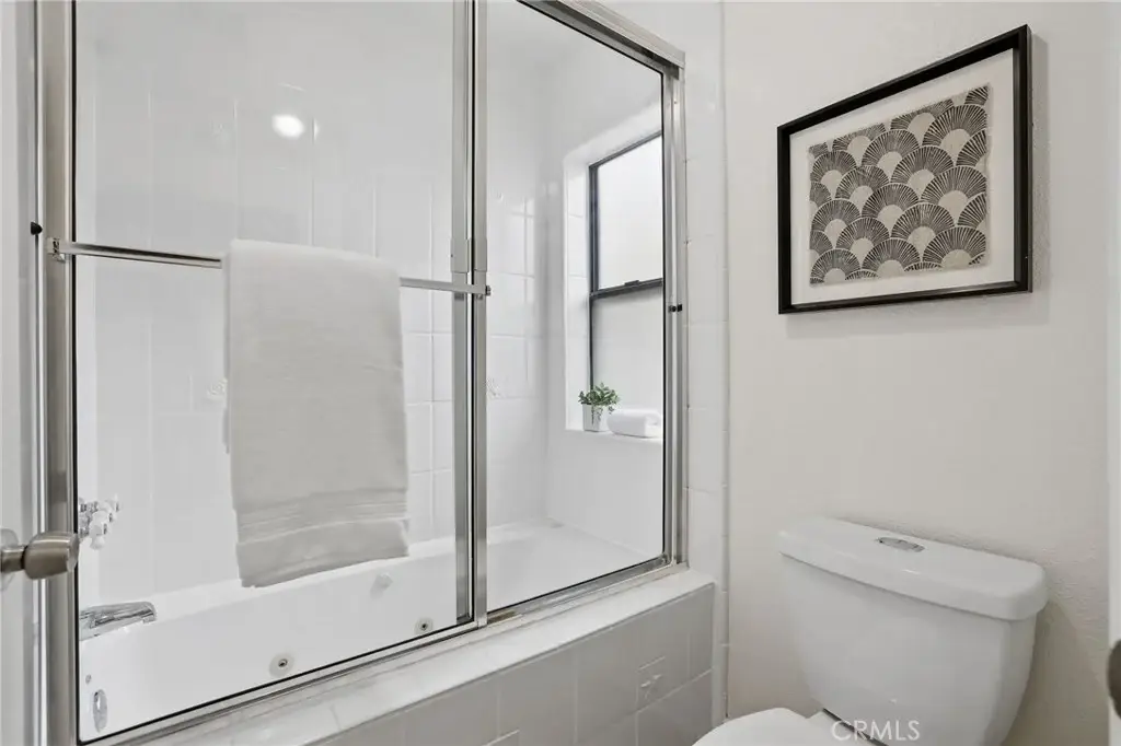 Bathroom with glass shower, bathtub, toilet, towel, plant, and framed artwork