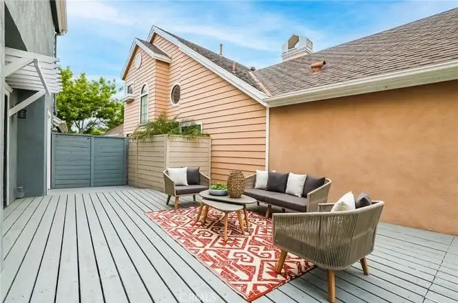Outdoor patio with gray decking, sofa, two armchairs, round table, and red patterned rug