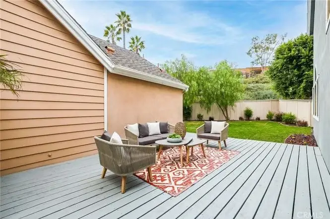 Backyard deck with gray wooden floor, outdoor sofa, chairs, table, and surrounding greenery