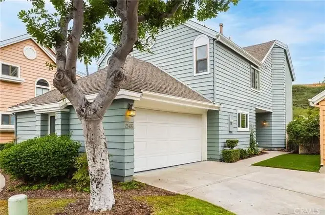 Two-story light blue house, California real estate, with driveway, surrounded by greenery and trees