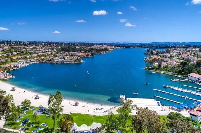 California lake with clear water, greenery, houses, boats, and sandy beach in foreground