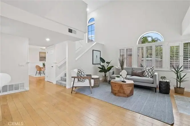 Living room with gray sofa, wooden coffee table, plants, area rug, and stairs to upper level