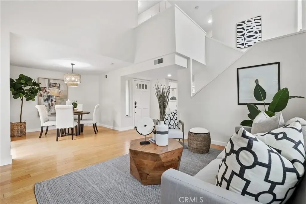 Living room with patterned sofa, wooden coffee table, plants, and dining area with round table and white chairs