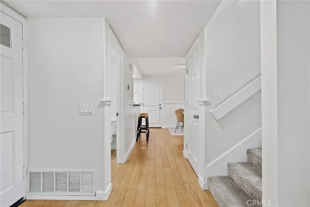Entryway with light wood floors, staircase, hallway, and view of kitchen with stools and table