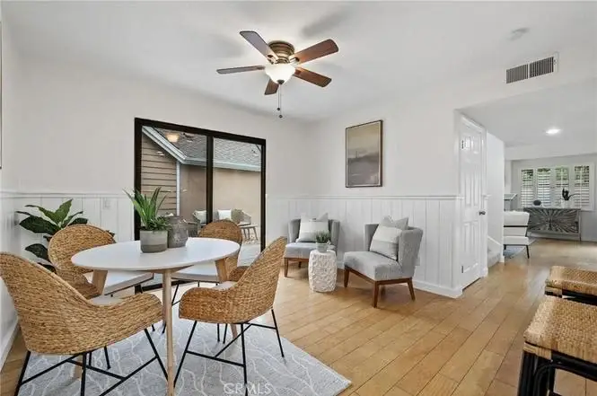 Dining area with round table, four wicker chairs, ceiling fan, windows, and decorative plants