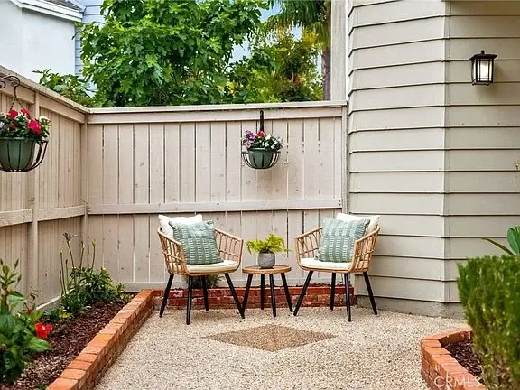 patio with two chairs, round table, plants, wooden fence, and hanging flower pots.